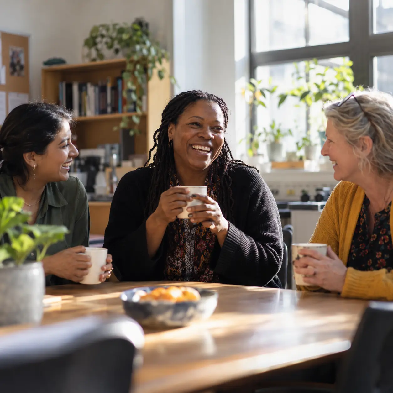 Three teachers laughing together over cups of tea in the staff room